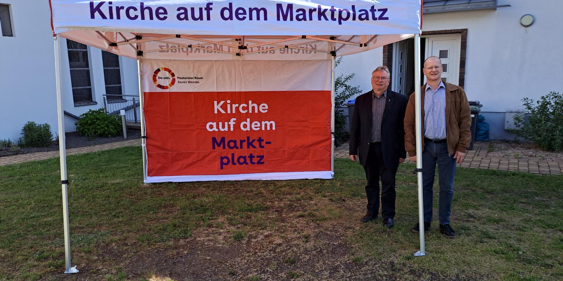 Man sieht ein Faltzelt und zwei Menschen, im Hintergrund ein Gebäude.