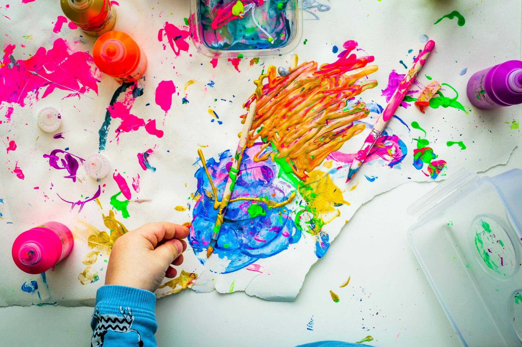 Eine Kinderhand, verschiedene Farben und Pinsel im Hintergrund