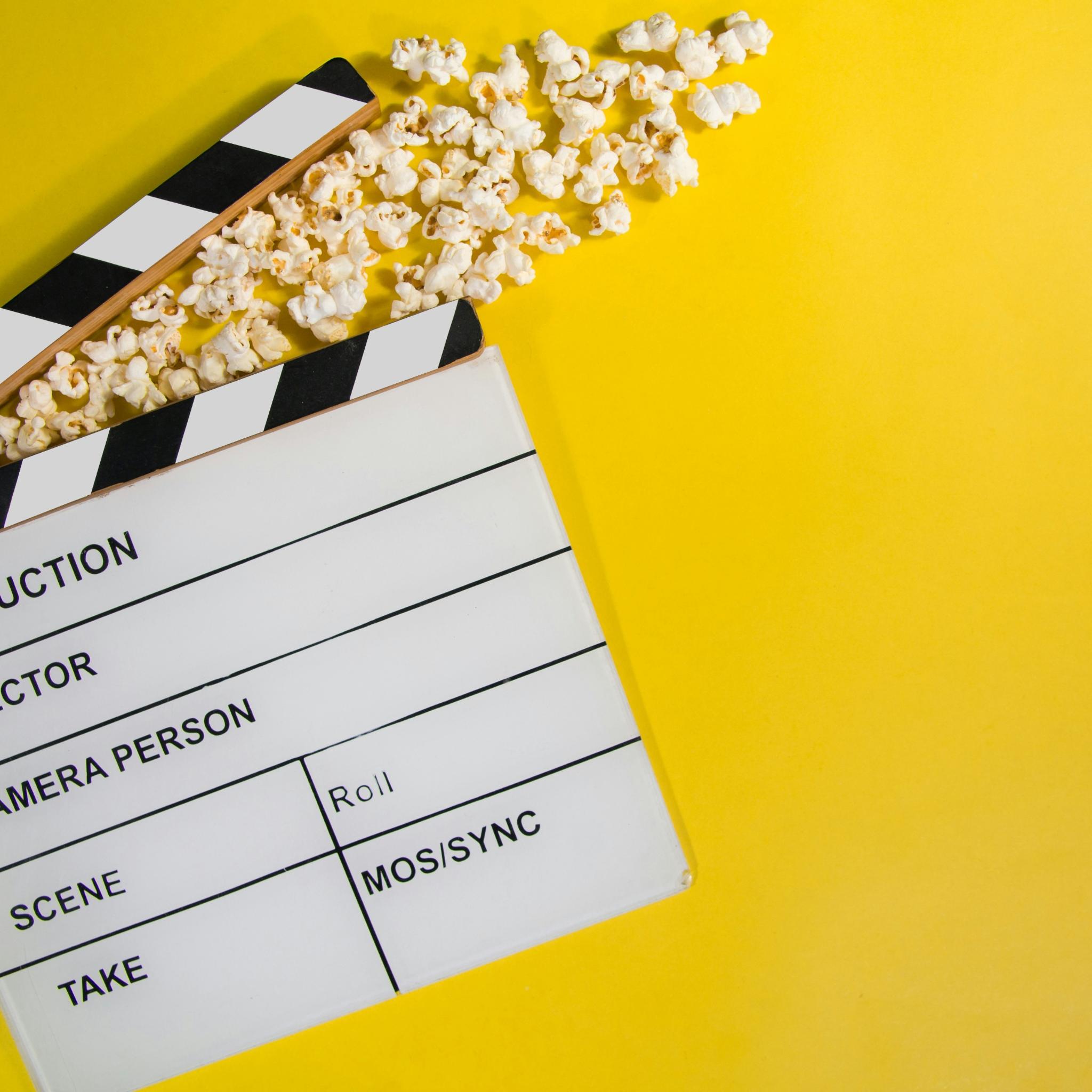 gelber Hintergrund, eine Filmklappe mit Popcorn (c) https://unsplash.com/de/fotos/weisses-druckerpapier-mit-schwarzen-texten-q8P8YoR6erg gelber Hintergrund, eine Filmklappe mit Popcorn