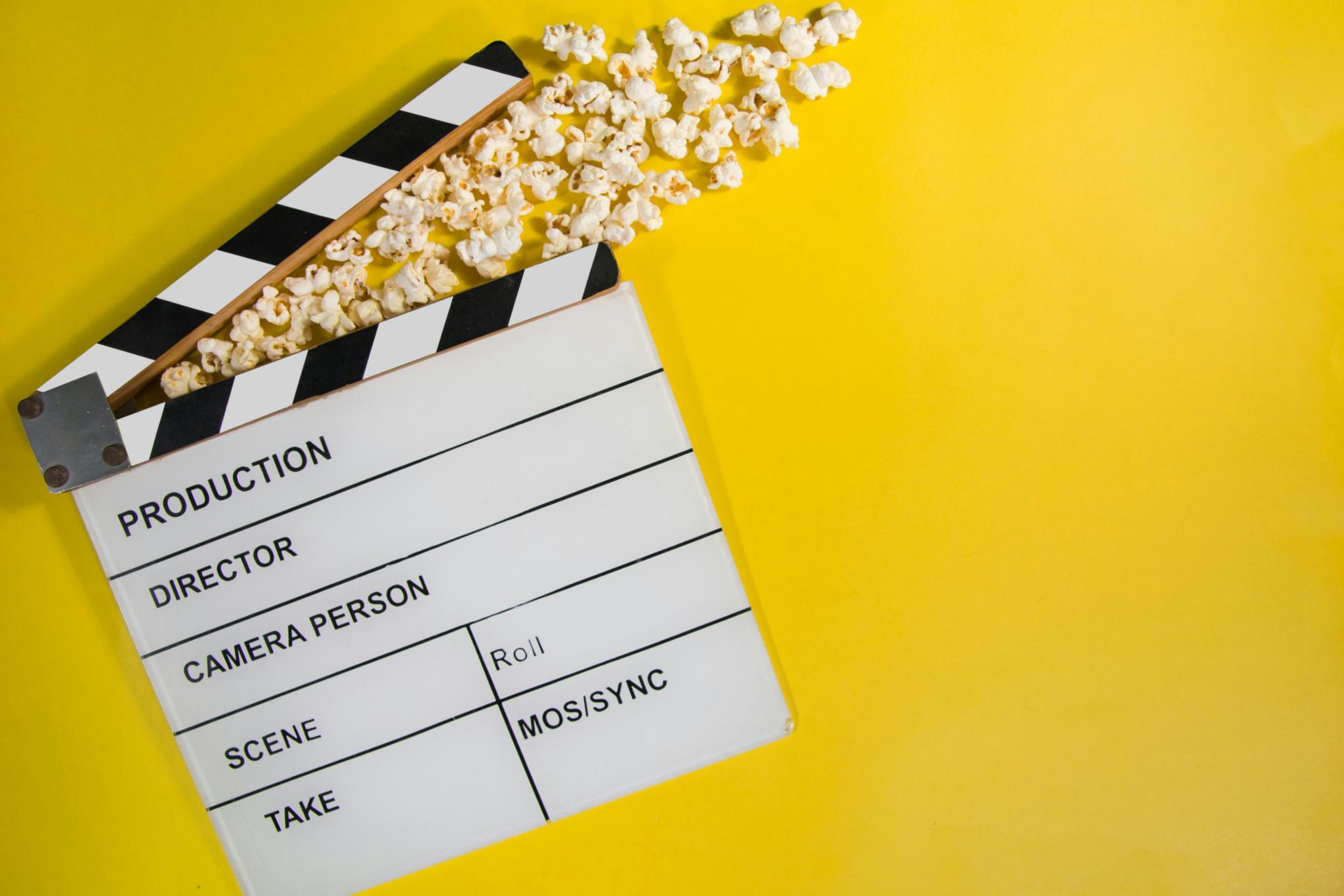 gelber Hintergrund, eine Filmklappe mit Popcorn (c) https://unsplash.com/de/fotos/weisses-druckerpapier-mit-schwarzen-texten-q8P8YoR6erg gelber Hintergrund, eine Filmklappe mit Popcorn