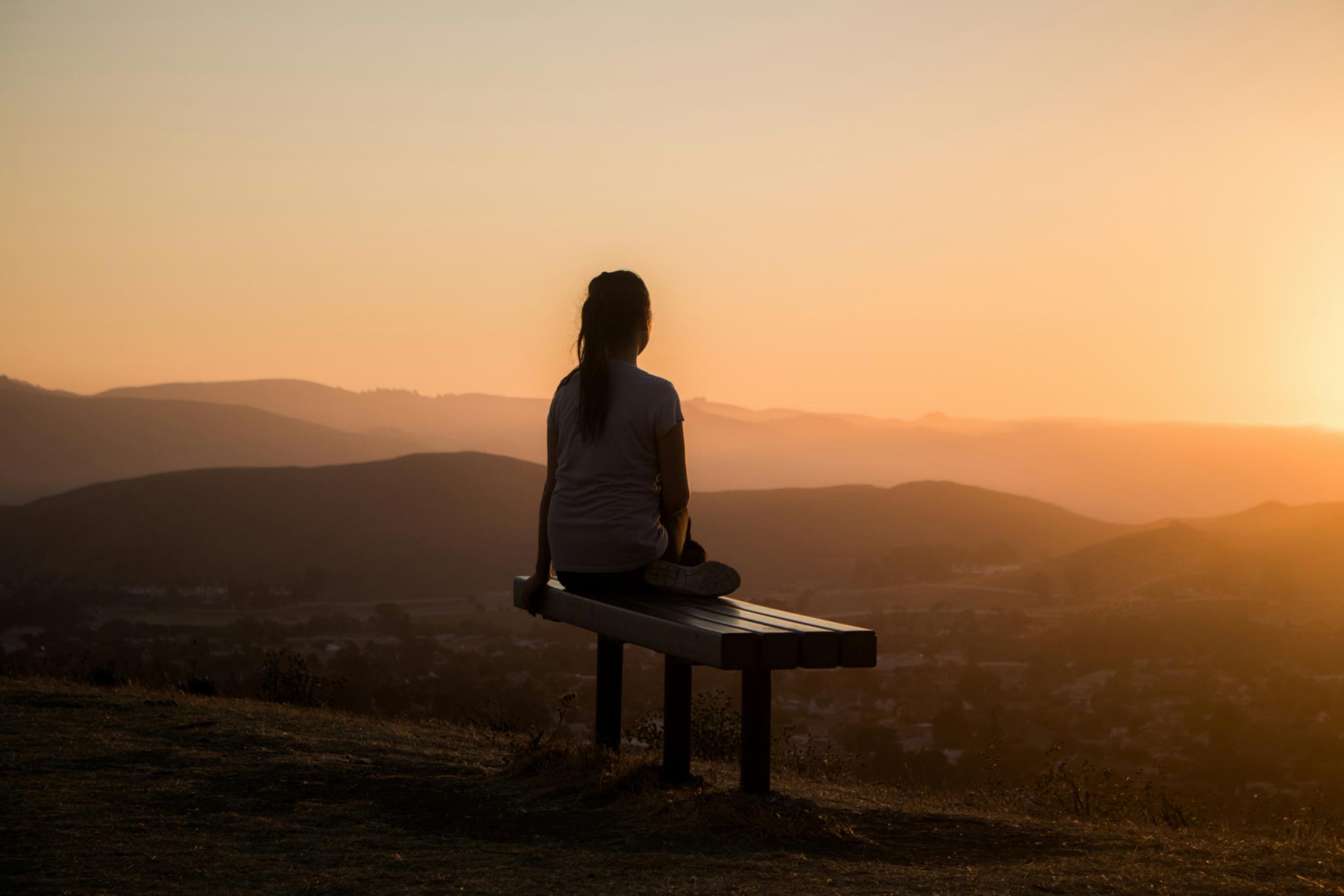 Frau sitzend auf einer Bank, Im Hintergrund Sonnenaufgang