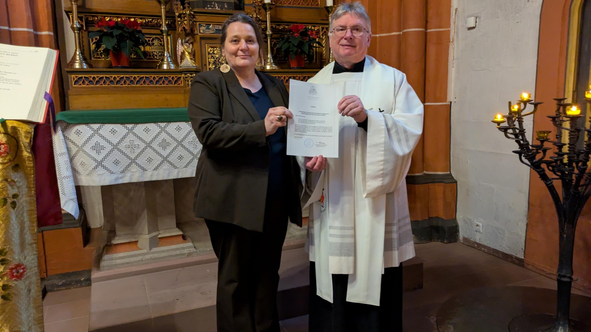 Vor dem Marienaltar der Basilika St. Wendel stehen Dekan Leist und Monika Leidinger mit einer Urkunde