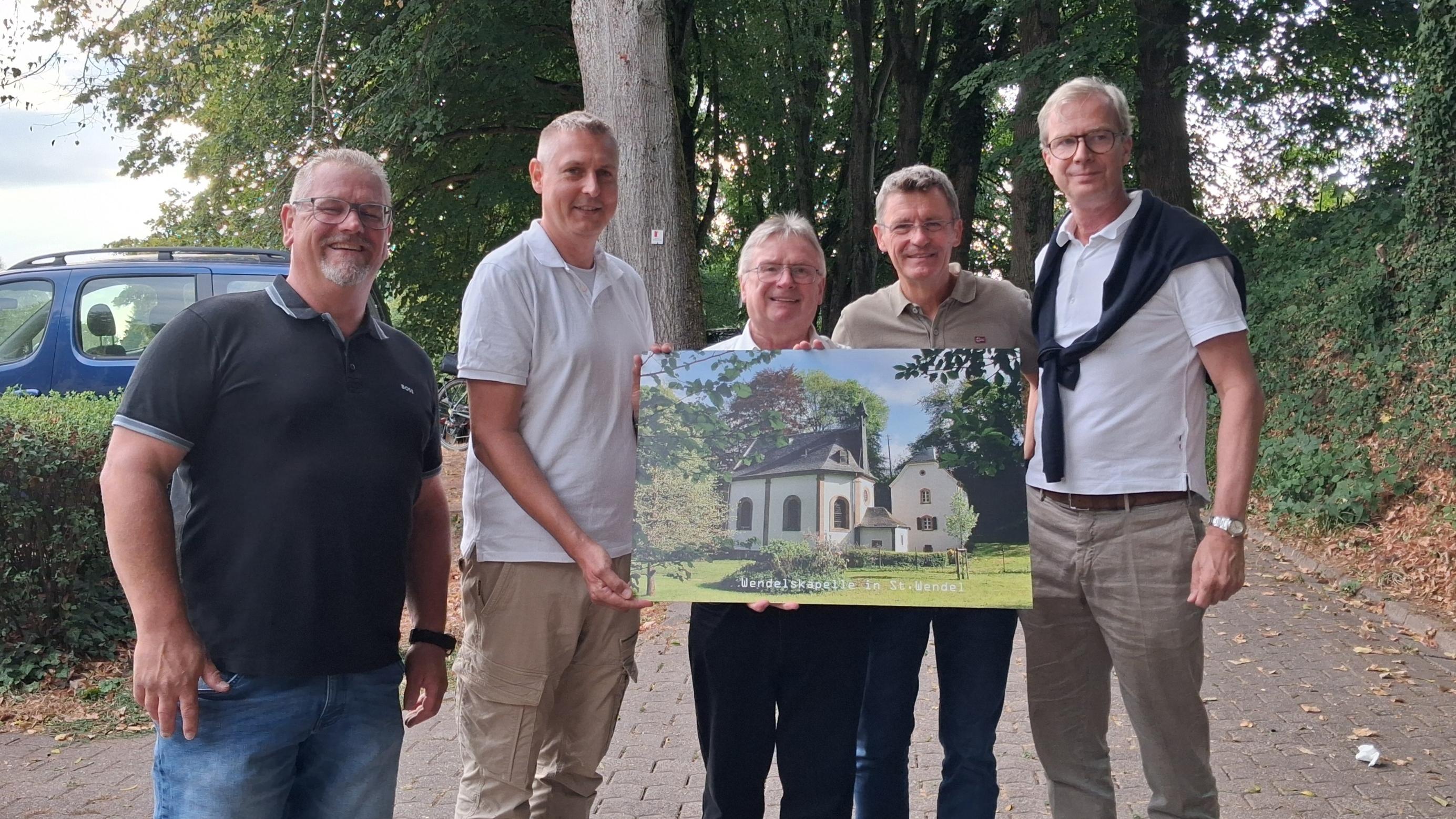 Bürgermeister und Ortsvorsteher überreichen Pastor ein Bild der Wendelskapelle